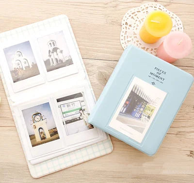 A light blue compact photo album with a lid open, displaying instant film photos and next to a yellow candle.