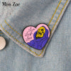 A heart-shaped enamel pin featuring a skull with purple shading and the text Live Laugh Love pinned on denim fabric.