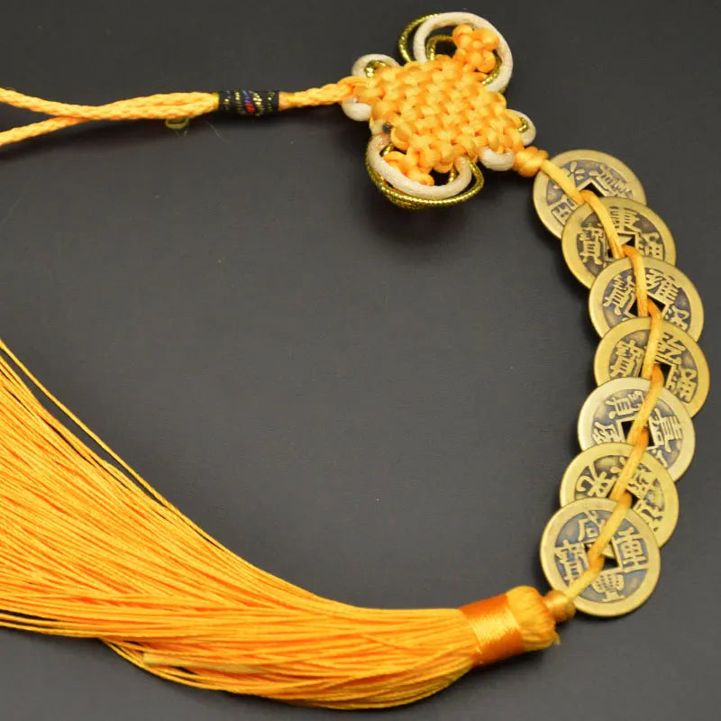 A yellow copper coin charm with a handwoven knot is displayed on a thin orange thread.