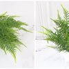 A sprig of bright green artificial fern leaves displayed on a white marble surface.