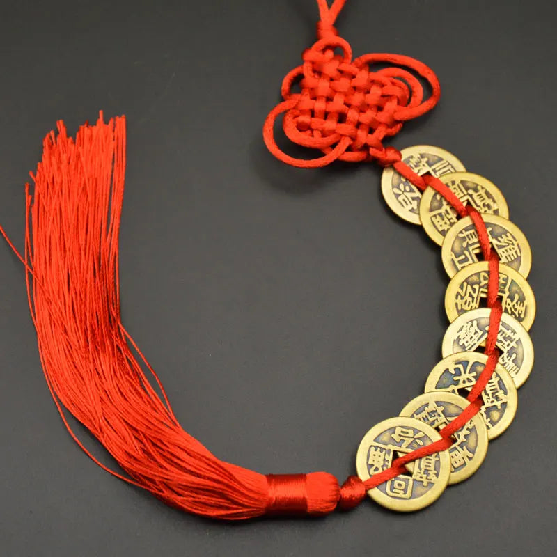 A red thread charm featuring a handwoven knot and several round copper coins used as an I Ching Feng Shui charm.