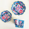 A set of colorful floral disposable tableware featuring pink, purple, and blue flowers on a light background.
