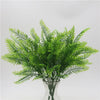 A vibrant green artificial fern with delicate fronds displayed in a clear glass vase.