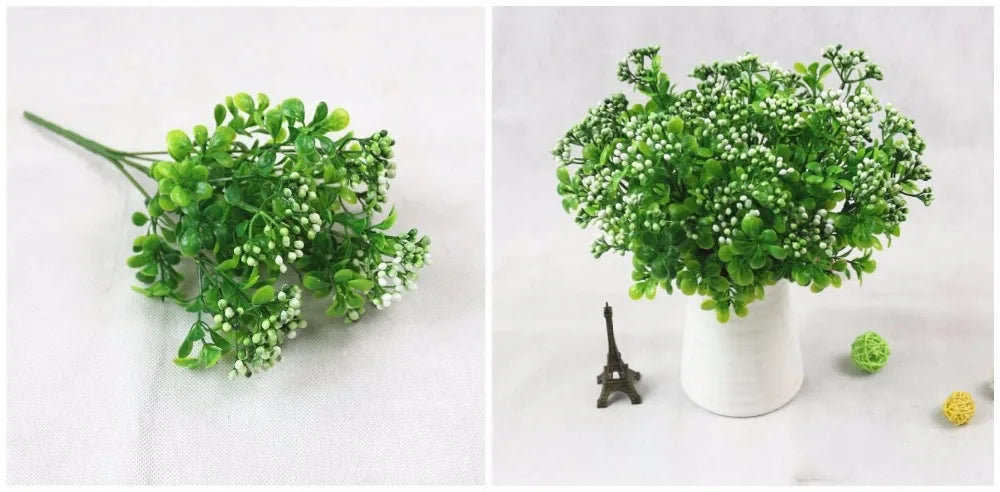 A close-up of vibrant green artificial fern and leaf sprigs with small white flowers displayed in a white vase.