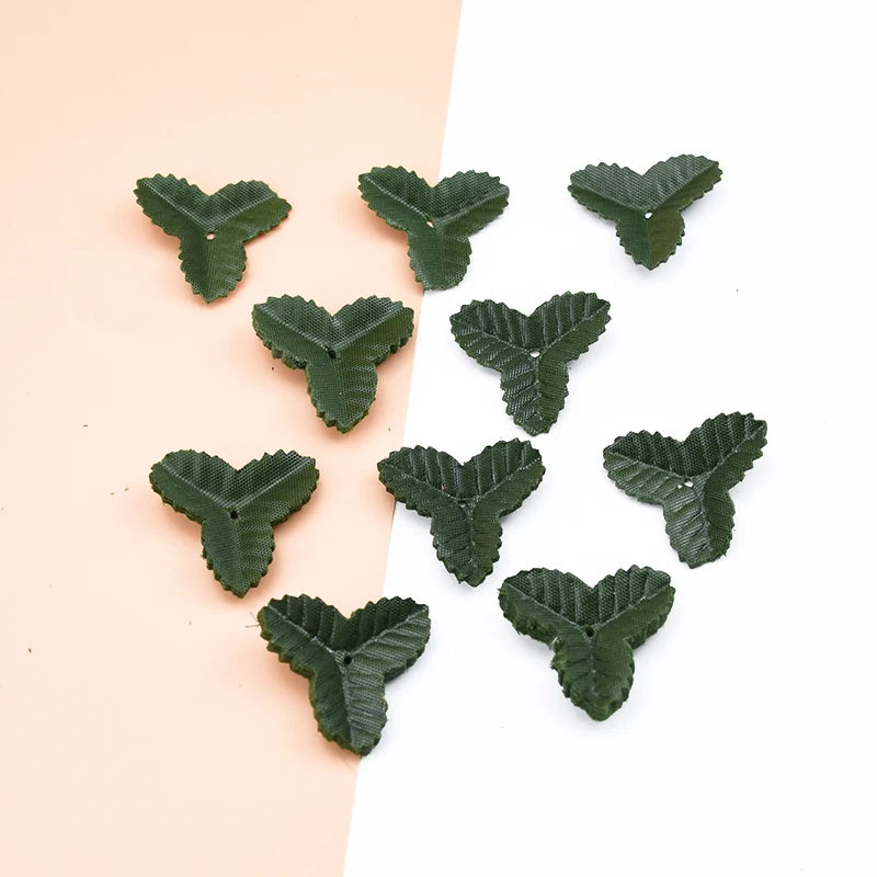 A collection of small, artificial green leaves scattered on a light pink and white background.