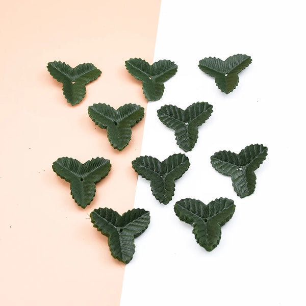 A collection of small, artificial green leaves scattered on a light pink and white background.