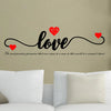 A black script word love with red hearts above it on a beige wall.