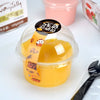A clear plastic dessert cup filled with yellow fruit puree, next to a pink container and a black fork.
