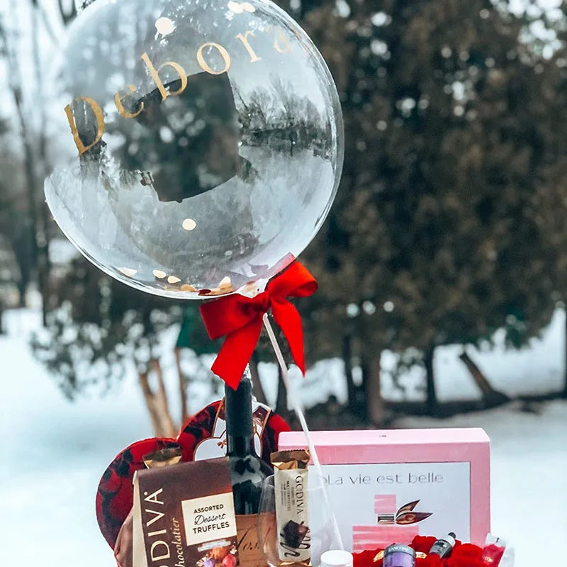 A clear balloon with the name Deborah is tied with a red ribbon, surrounded by various small products.