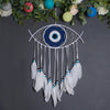 Handmade boho evil eye dream catcher with white feathers and blue mandala design hanging from green foliage