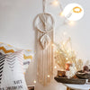 Boho macrame dream catcher wall decor featuring cream-colored macrame and string lights on a white wall.