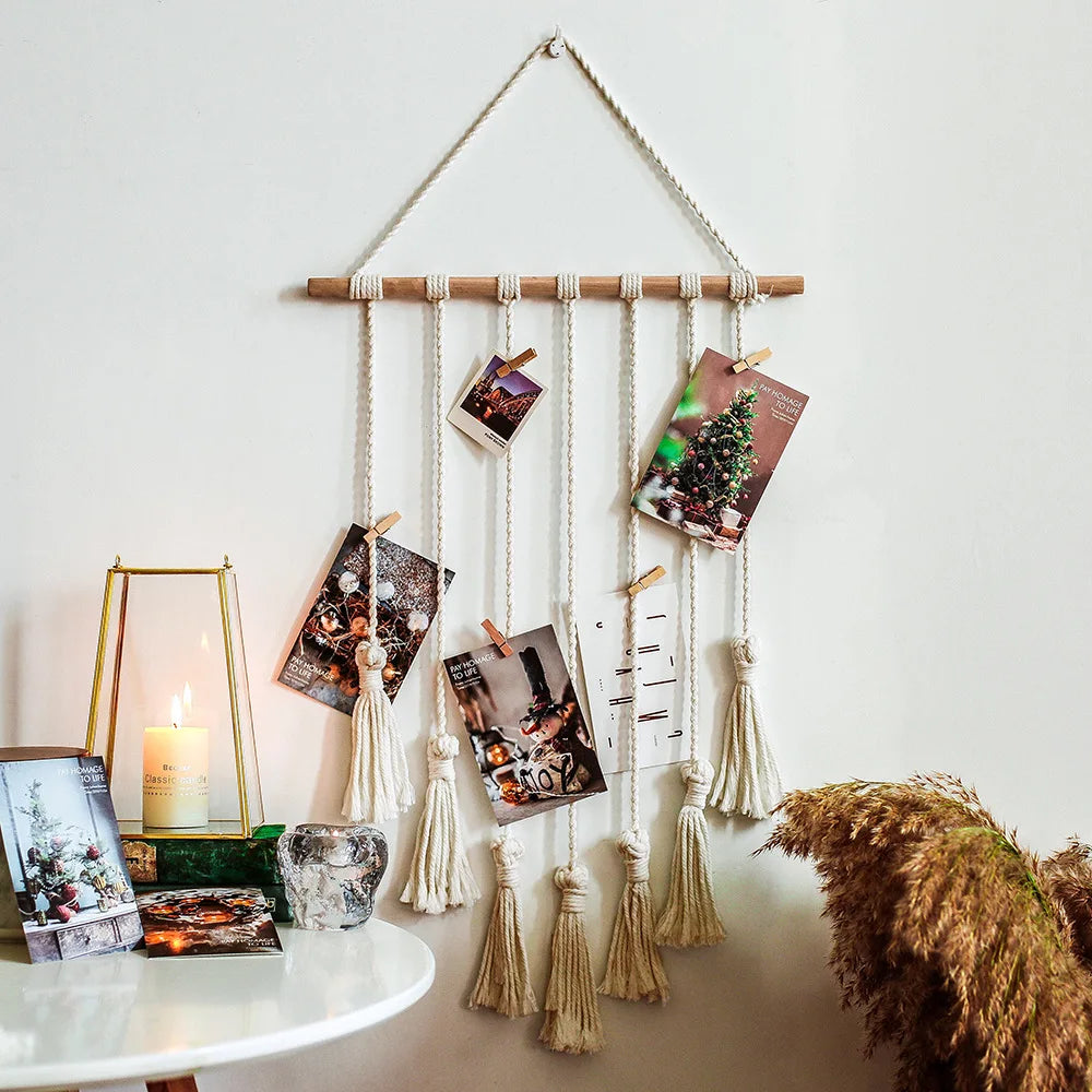 A macrame photo display featuring multiple framed photos hanging from a wooden rod against a white wall.