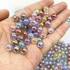 A hand holds a cluster of iridescent, round acrylic beads in various shades of purple, pink, and gold for jewelry making.