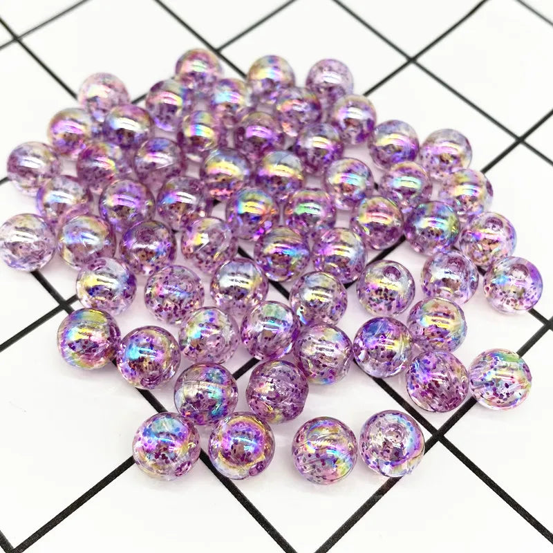 A pile of iridescent purple acrylic round beads for jewelry making scattered on a grid background.