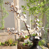Artificial silk cherry blossom branches with white and pink flowers displayed in a rustic indoor setting.