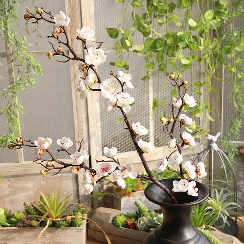Artificial silk cherry blossom branches with white and pink flowers displayed in a rustic indoor setting.