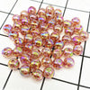 A pile of small, round, iridescent pink and gold acrylic beads for jewelry making