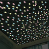 A ceiling decorated with glow-in-the-dark star and moon wall stickers in various pastel colors against a dark background.