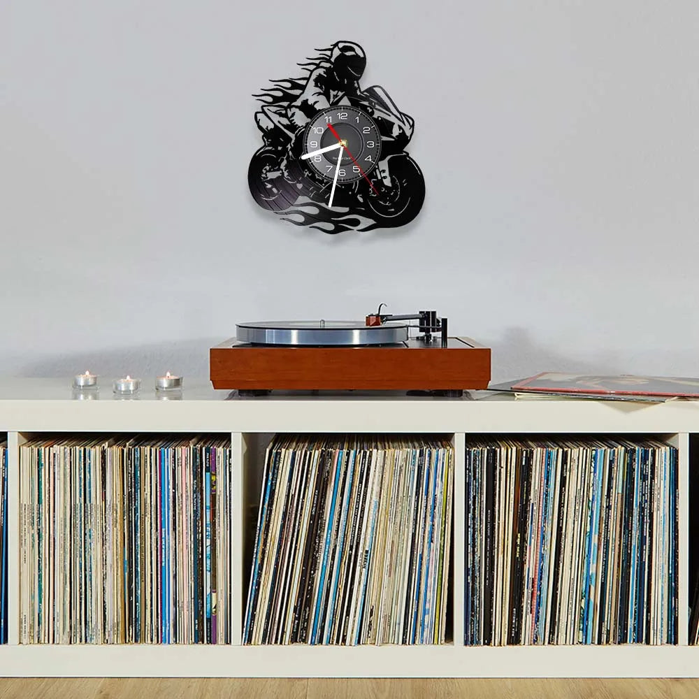 A motorcycle rider vinyl record wall clock mounted on a light gray wall above a wooden shelf displaying vinyl records.
