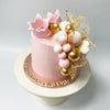 A pink buttercream cake decorated with white and gold floral elements and butterfly toppers.