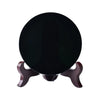 A round, polished black obsidian mirror resting on a wooden stand.