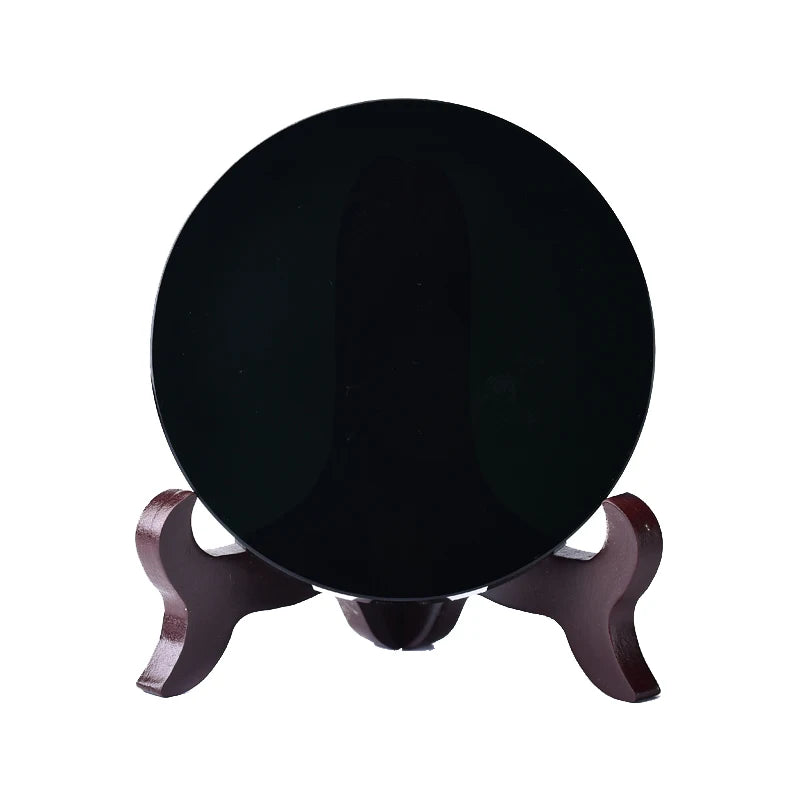 A round, polished black obsidian mirror resting on a wooden stand.