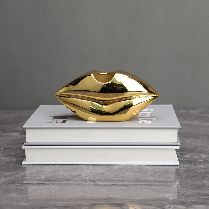 A shiny gold sculpture of a human lip shape rests on a stack of white books.