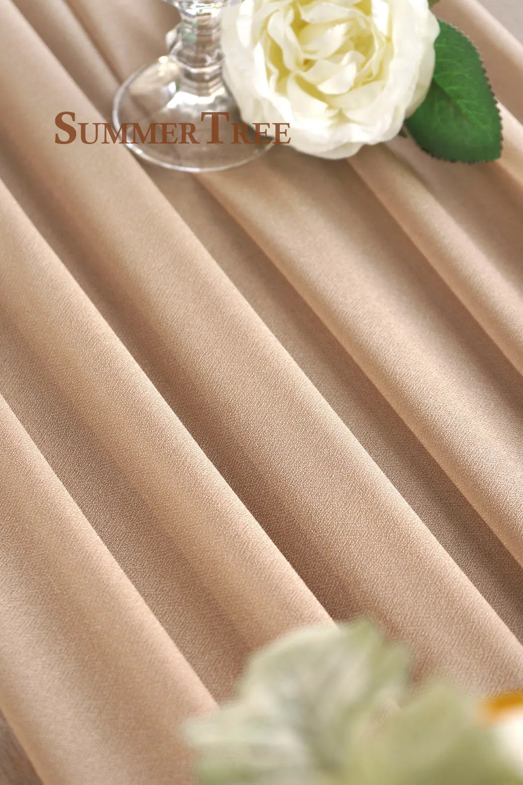 Elegant chiffon wedding arch drape fabric in a beige tone with a glass candle holder and green leaves.