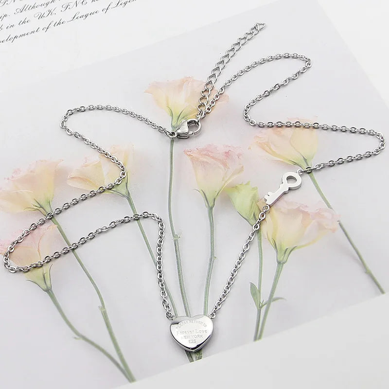 Silver titanium steel heart lock key pendant necklace displayed on a white background with pink roses.