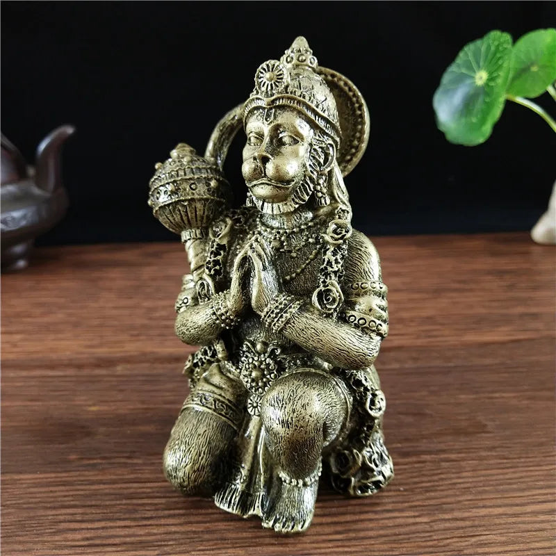 Bronze Hanuman statue figurine of a monkey god seated in a devotional pose on a wooden surface.