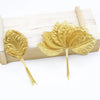 A set of twelve gold silk leaf artificial plant stems with vases displayed on a wooden board.
