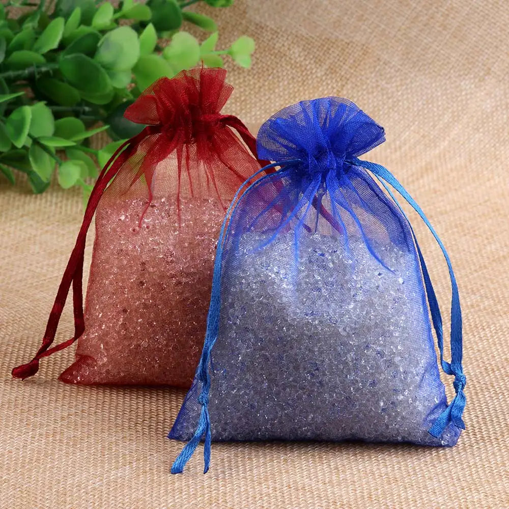 Two organza drawstring gift pouches in shades of pink and blue resting on a beige fabric.