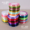 A stack of 6mm satin ribbon rolls in various colors, including green, gold, pink, and blue.