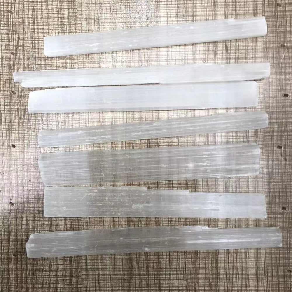 Several translucent white selenite crystal wands laid diagonally on a wooden surface.
