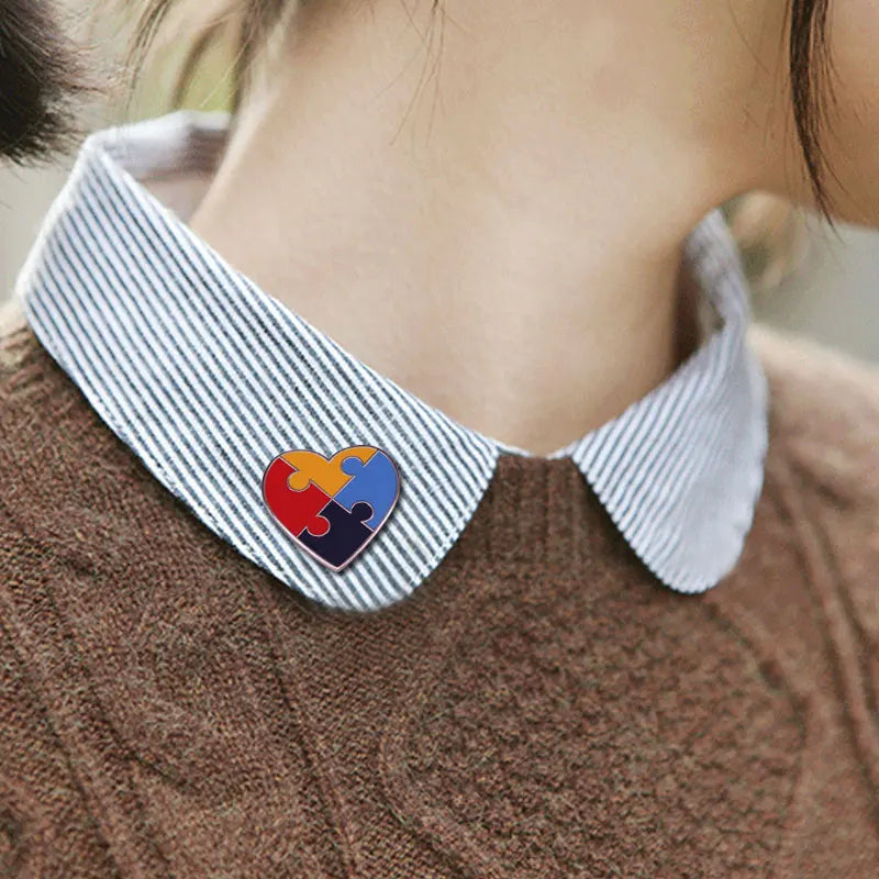A close-up of a blue and white striped shirt collar featuring a heart-shaped puzzle ribbon brooch pin.
