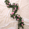 A lush green silk rose hanging vine garland with pink roses draped across sheer white fabric.