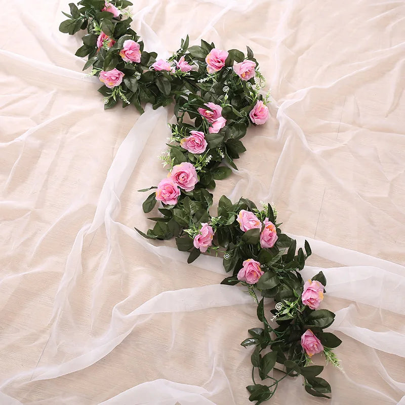 A lush green silk rose hanging vine garland with pink roses draped across sheer white fabric.