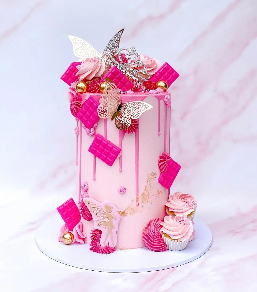 A pink cake decorated with pink and silver butterfly toppers and dripping icing on a white cake stand.