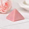 Cristal piramidal de fluorita rosa natural sobre una superficie blanca con pétalos de rosa rosados desenfocados al fondo.