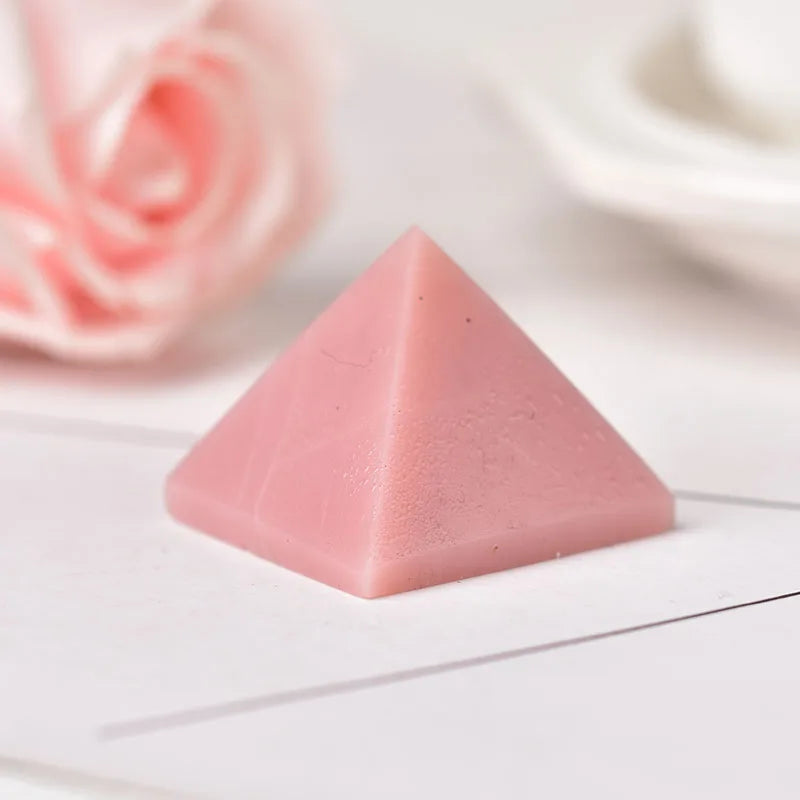 Cristal piramidal de fluorita rosa natural sobre una superficie blanca con pétalos de rosa rosados desenfocados al fondo.