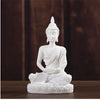 White resin Buddha statue with a serene expression seated in meditation on a round base.