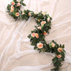 A green silk rose hanging vine garland with peach and pink roses draped on sheer white fabric.