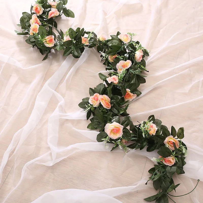 A green silk rose hanging vine garland with peach and pink roses draped on sheer white fabric.