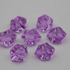 Several faceted purple acrylic crystals of various sizes are scattered on a white surface.