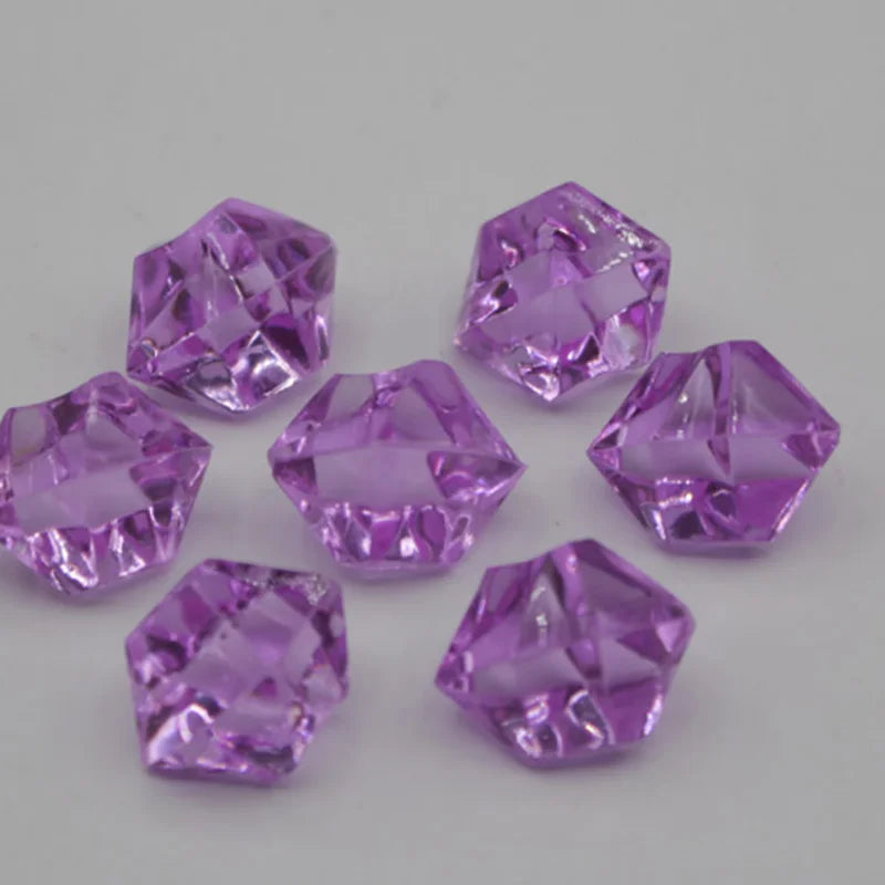 Several faceted purple acrylic crystals of various sizes are scattered on a white surface.
