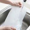 Hands are pouring water into a reusable fine mesh nylon filter bag inside a metal container.