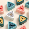 A collection of colorful, triangular suction cup towel holders and wall hooks in shades of pink, blue, yellow, and gray.