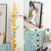 A vertical garland of colorful felt balls in various shades of yellow, green, pink, and white, displayed against a light back