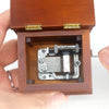 A wooden music box with a hinged lid open, revealing a silver hand-crank mechanism inside.