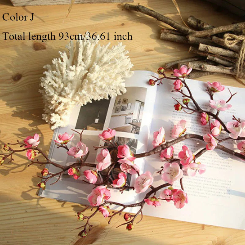 Artificial silk cherry blossom branches with a fluffy white accent displayed on a wooden surface.